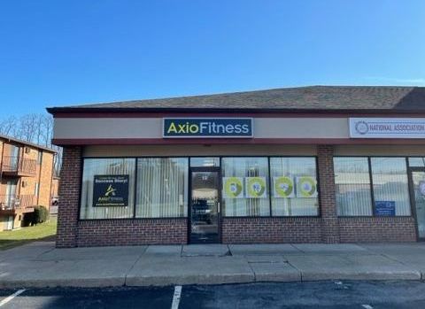 A storefront for Axio Fitness with a dark sign, glass windows, and a brick facade.