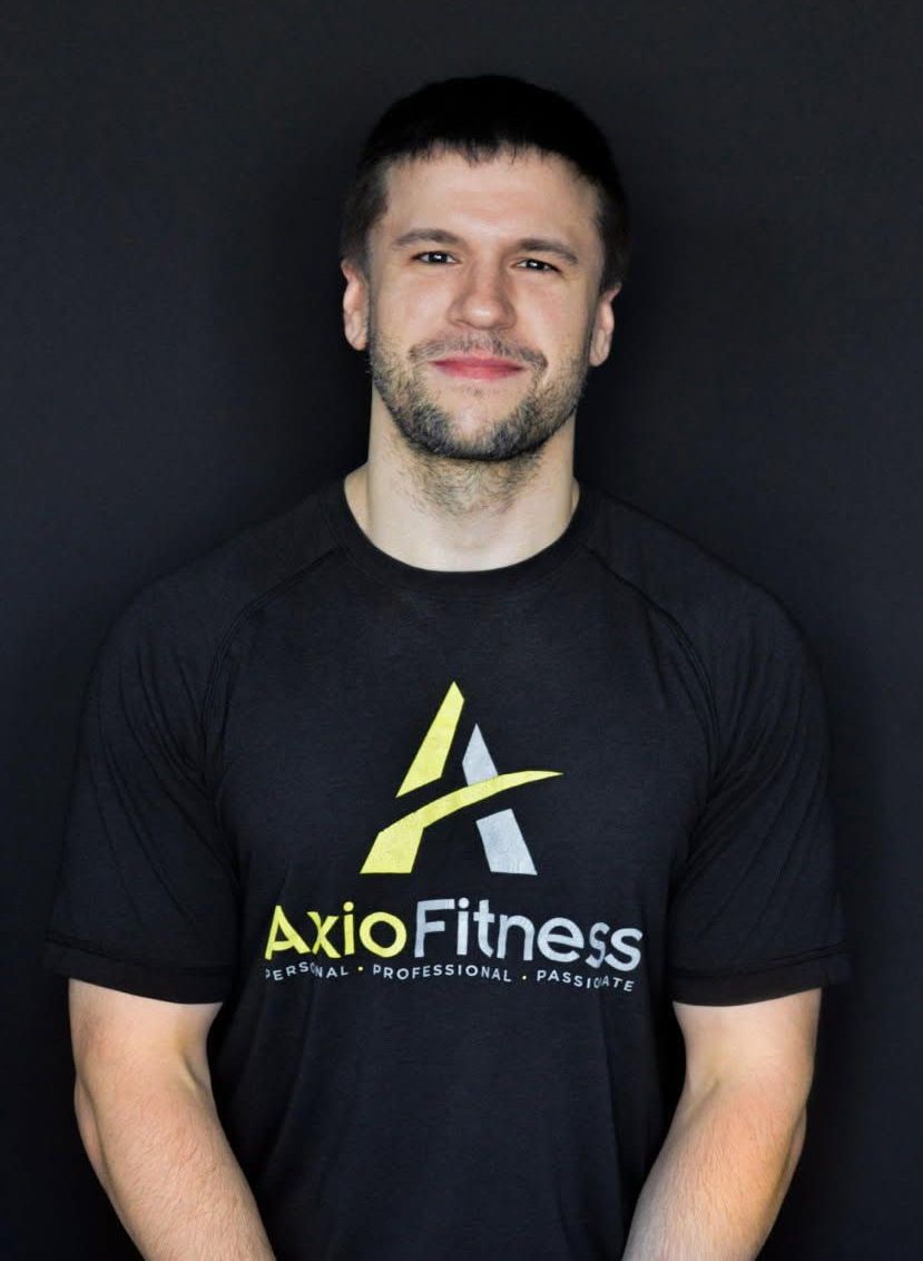 A man wearing a black AxioFitness t-shirt smiles in front of a black background.