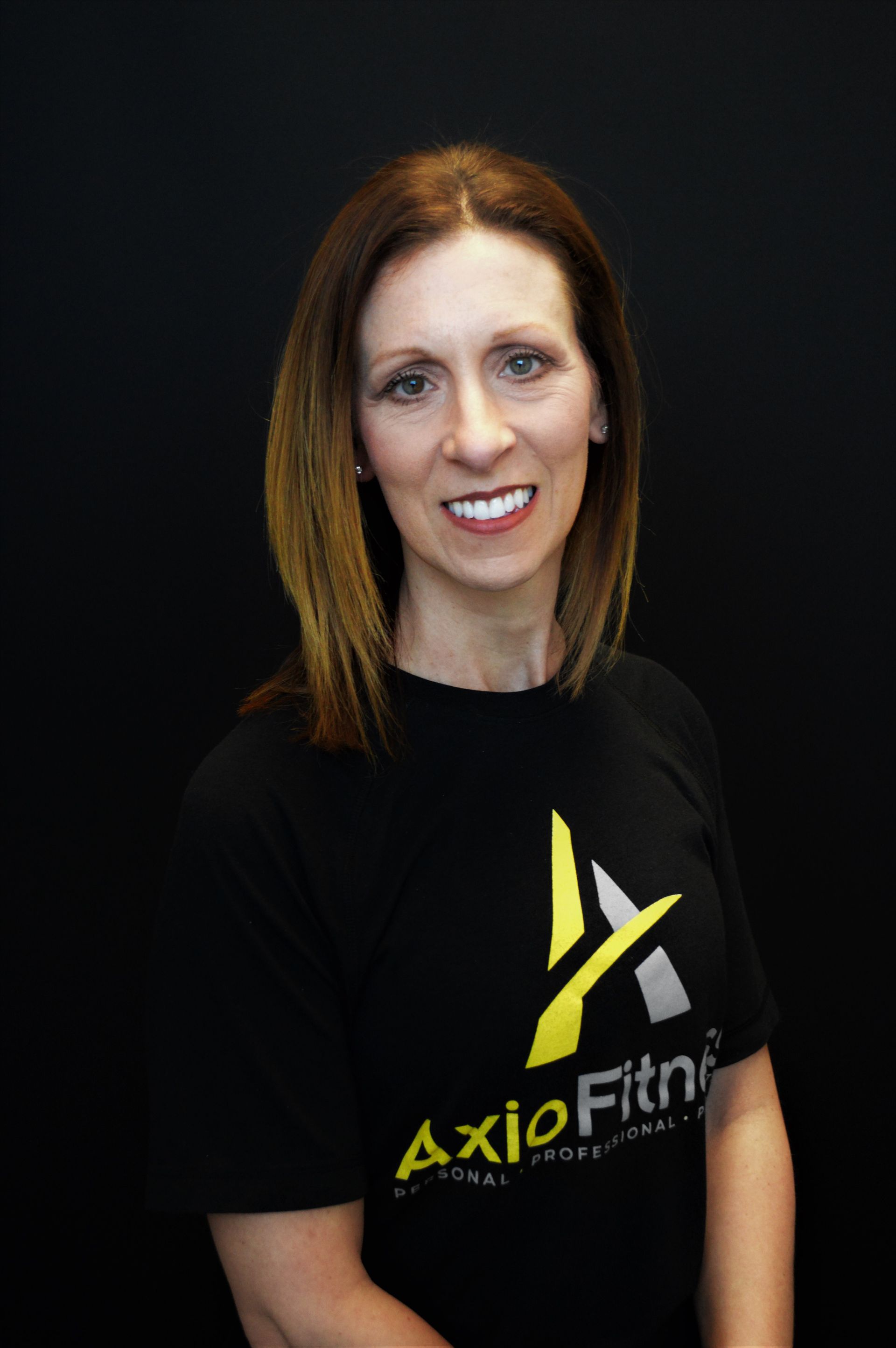 A Woman wearing a black AxioFitness t-shirt in front of a black background.