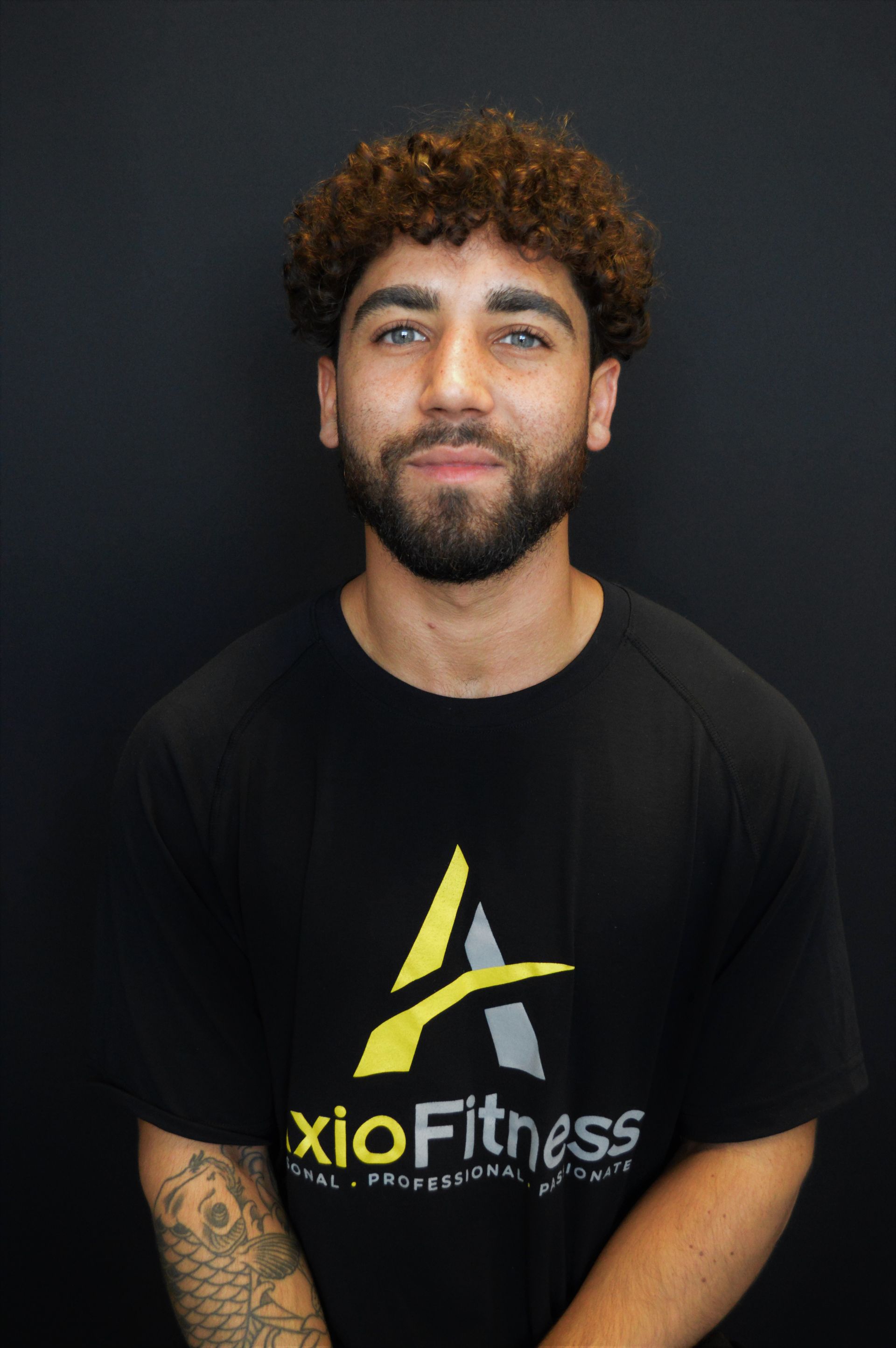 A man with curly brown hair and a beard smiles, wearing a black