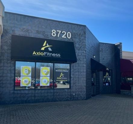 AxloFitness storefront with black awning and logo, address 8720 above. Gray brick building with windows displaying services.