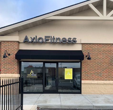 Axio Fitness storefront with a black awning and glass doors, featuring the business name in gray letters. Exterior view.