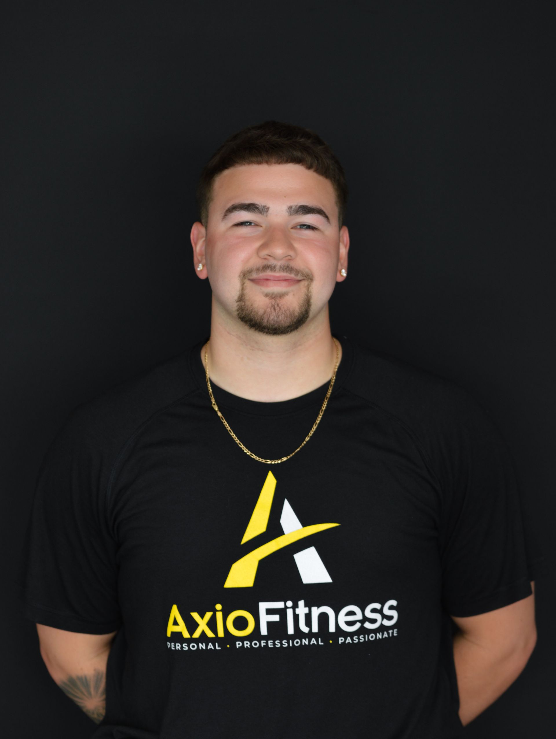 A young man in a black AxioFitness t-shirt smiles at the camera, dark background.