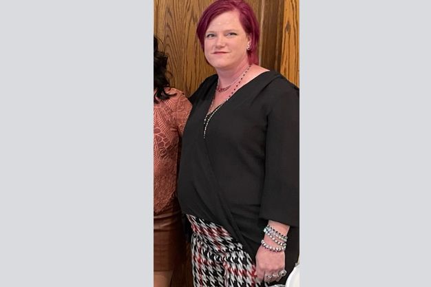 Woman with pink hair wearing a black top, patterned skirt, and bracelets. 