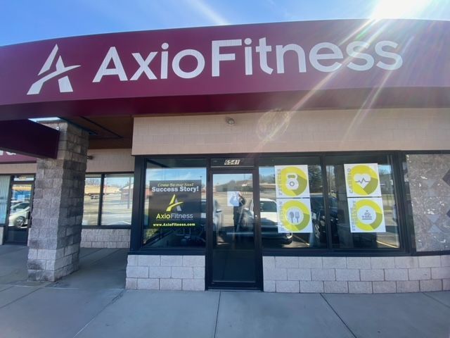 AxioFitness storefront with a maroon awning and large windows. The business logo is visible. 