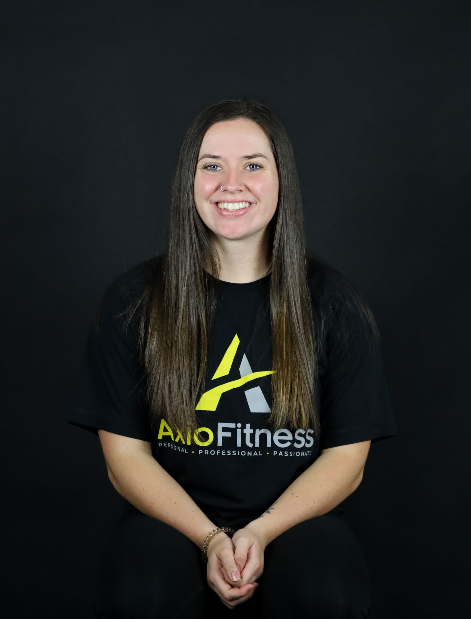 Woman with long brown hair, smiling, wearing a black t-shirt with the 