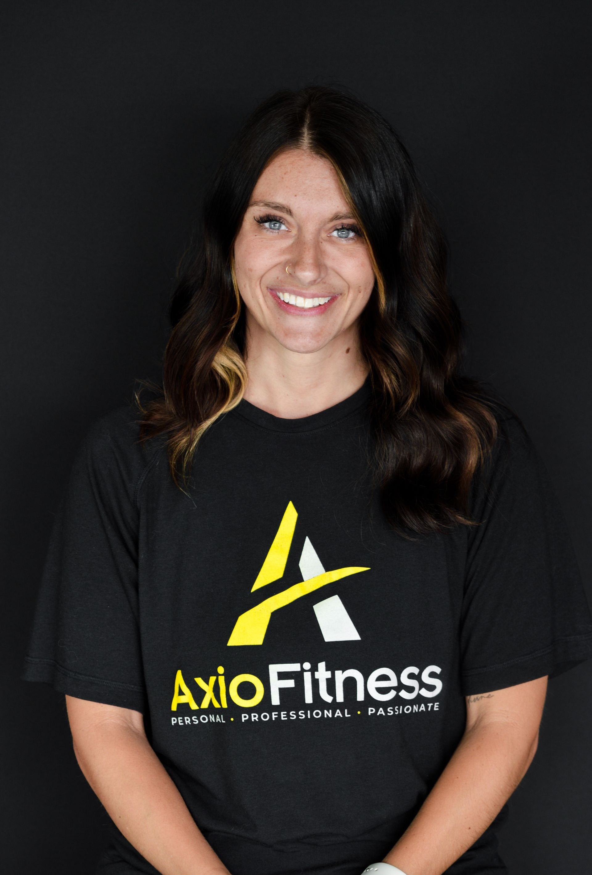 Woman in black AxioFitness T-shirt smiling against a dark background