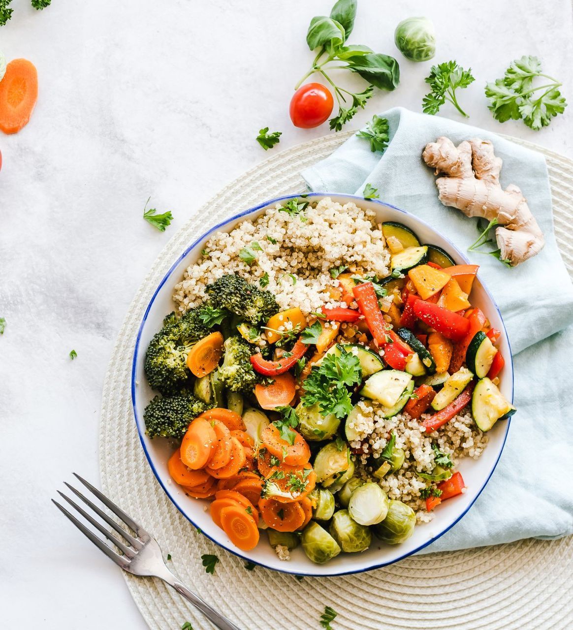 Healthy meal bowl with quinoa, roasted vegetables, and fresh herbs on a white surface.