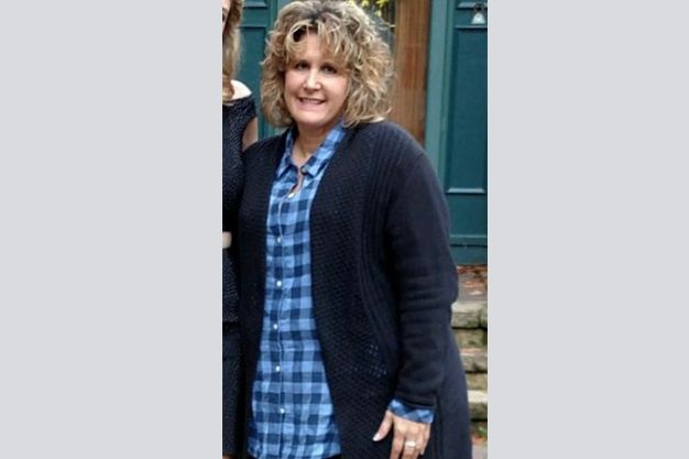 Woman with curly blonde hair, smiling, wearing a blue plaid shirt and a navy cardigan.