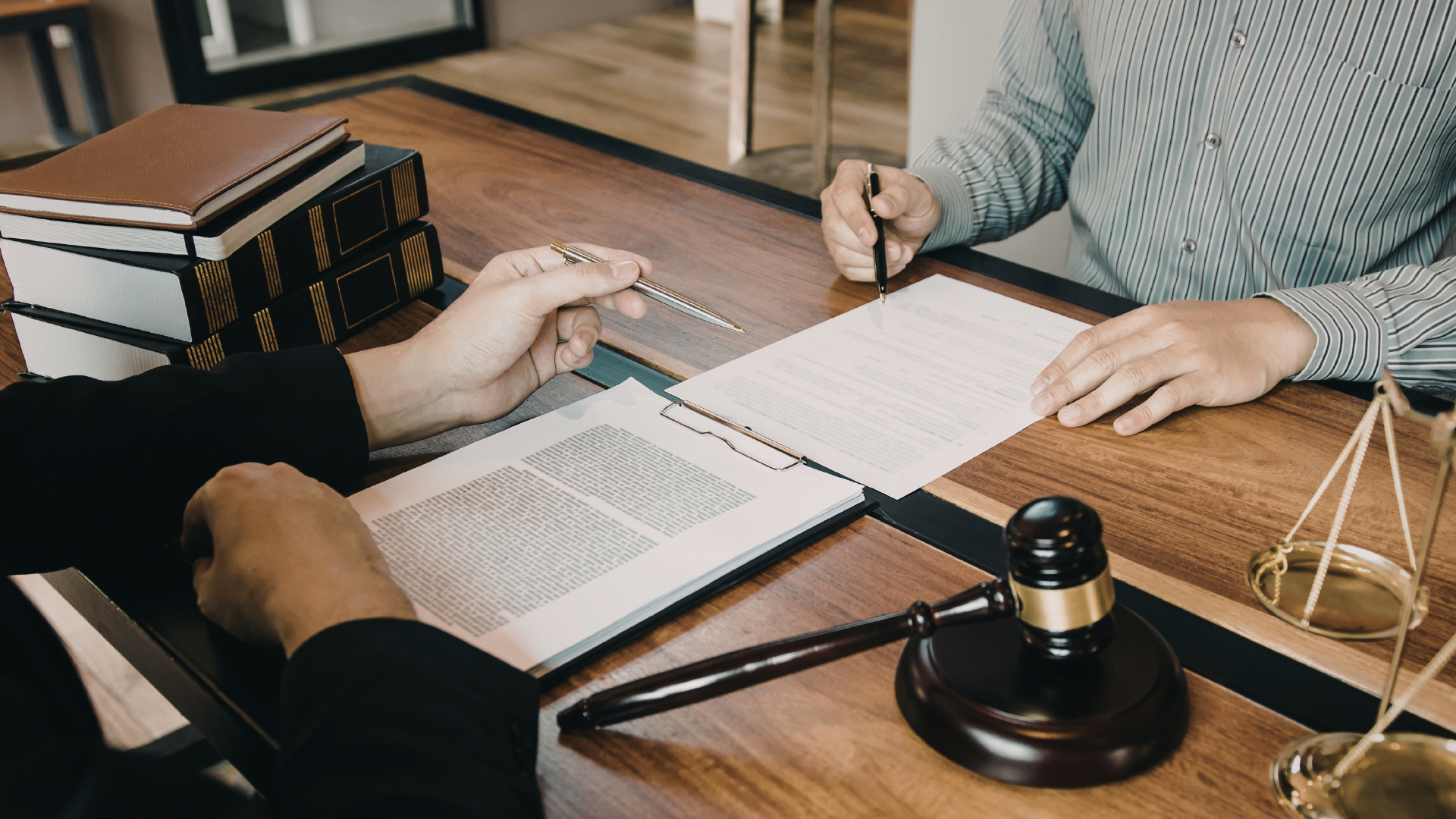 Two people review documents at a desk with a gavel and law books, suggesting a legal meeting.