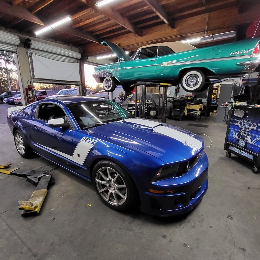 A blue mustang is parked in a garage next to a green car
