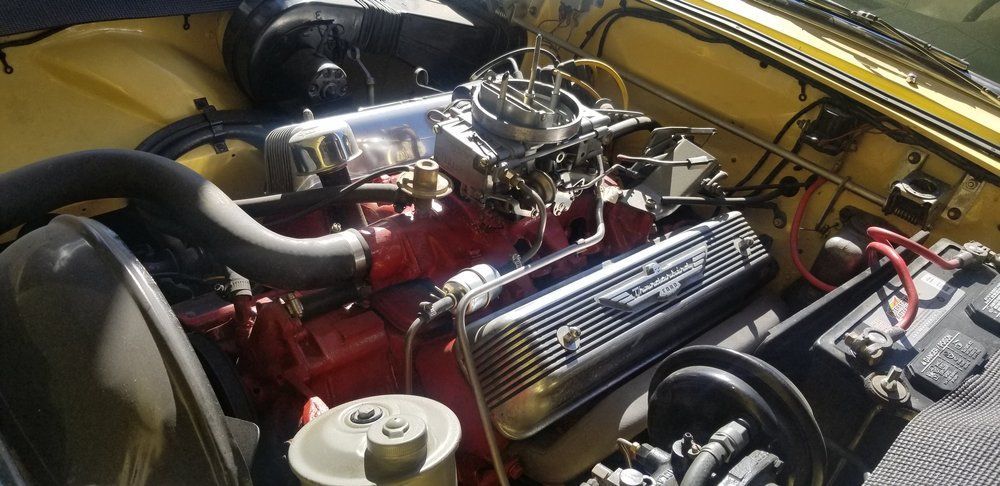 A close up of a car engine with a battery in the background.