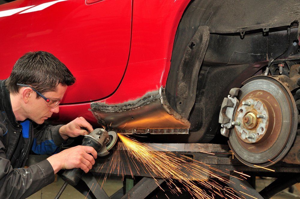 A man is grinding the side of a red car