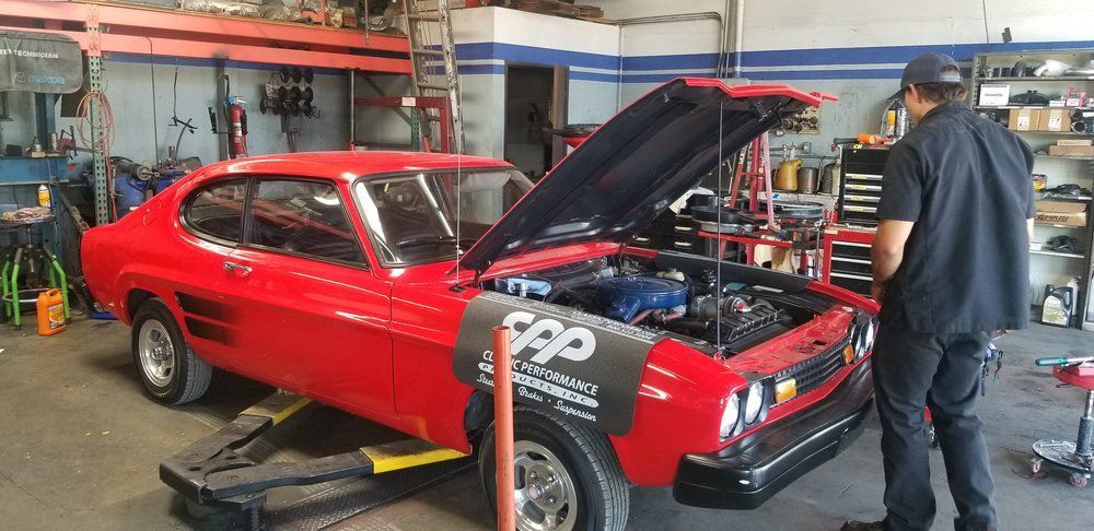 A man is standing next to a red car with the hood up in a garage.