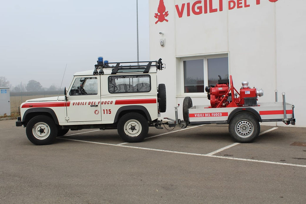 Camion dei pompieri bianco con rimorchio, parcheggiato di fronte a un edificio con la scritta italiana