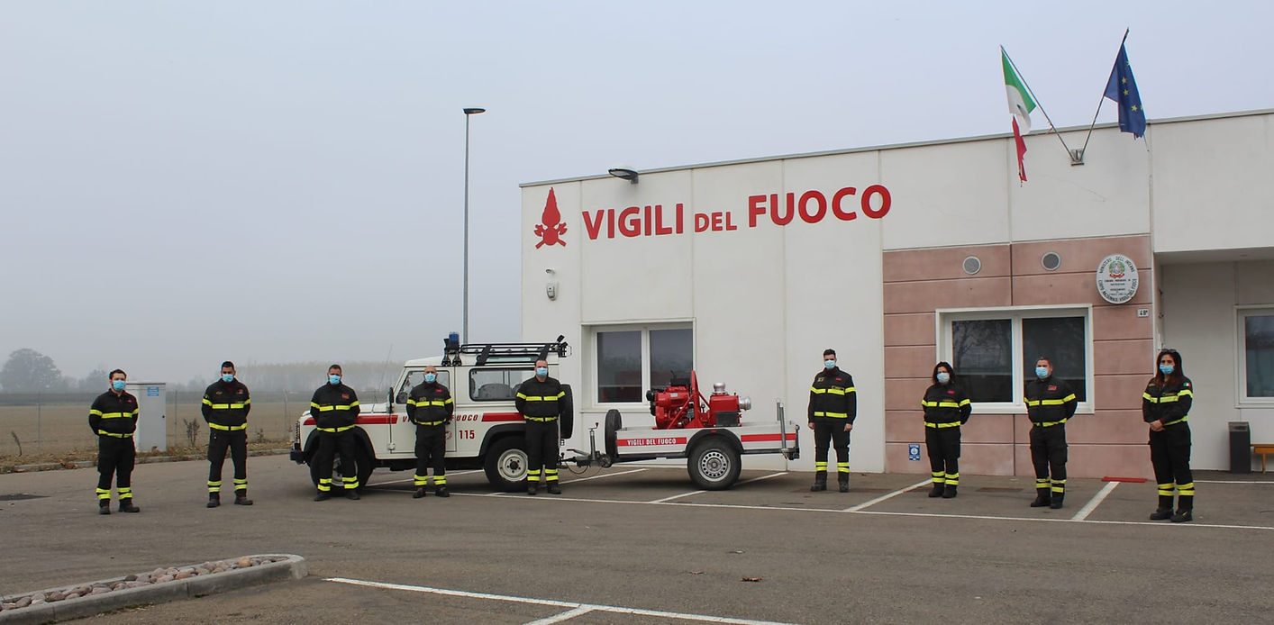 Vigili del fuoco in piedi davanti a una caserma dei pompieri con un'autopompa.
