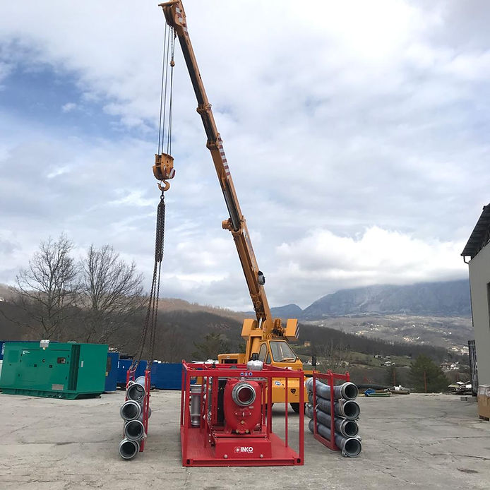 Gru che solleva un sistema di pompaggio rosso, con tubi flessibili collegati, all'aperto con montagne sullo sfondo.