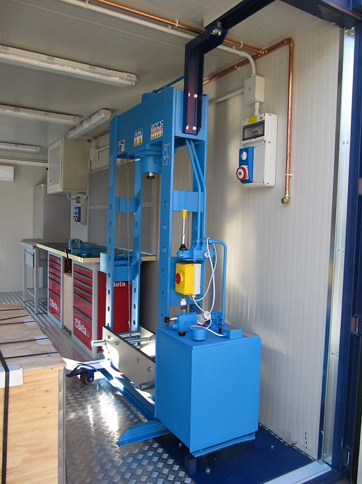 Pressa idraulica blu all'interno di un'officina. Sono visibili armadietti per attrezzi, banco da lavoro e attrezzature.