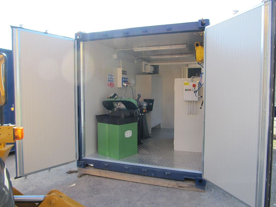 Officina container aperta con macchinari, luci e pareti bianche.