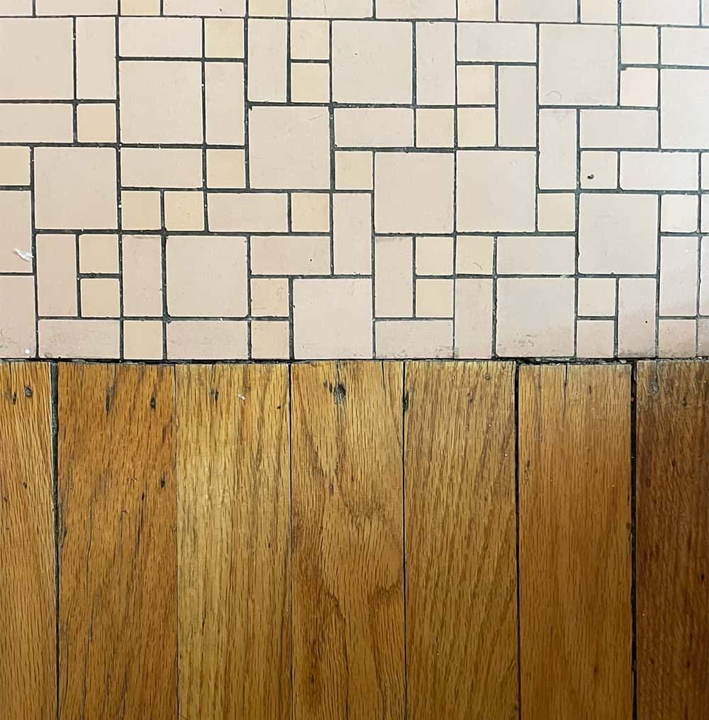 There is a wooden floor next to a tiled wall.