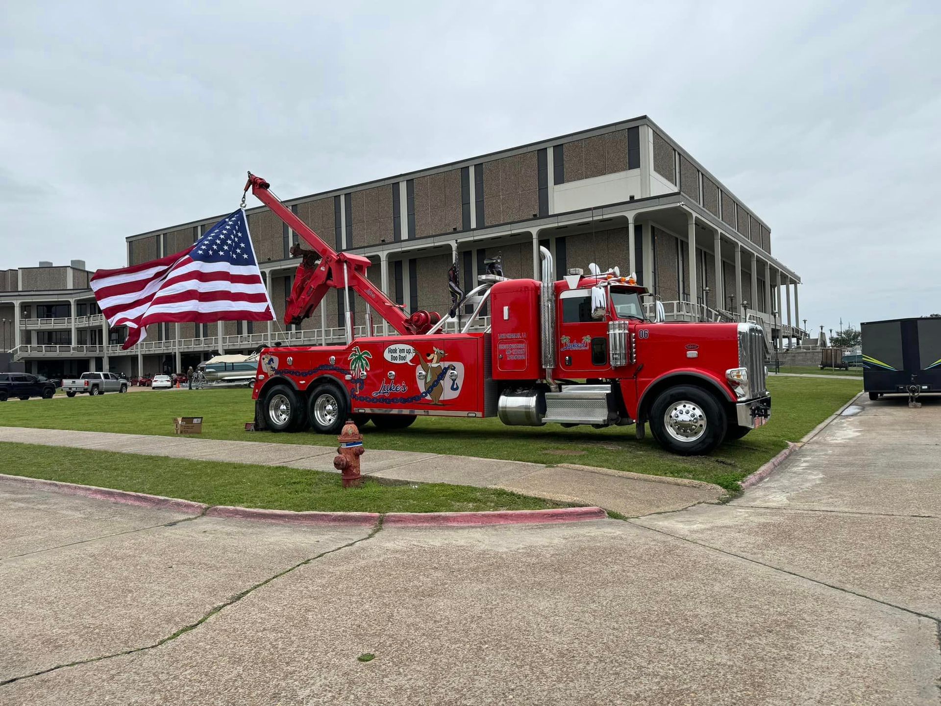 A red tow truck is parked in front of a building with an american flag.