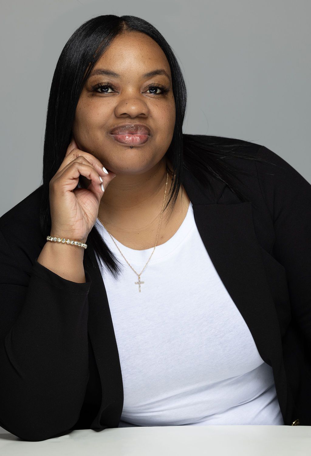 Portrait of a woman in a black blazer and white top, resting her chin on her hand against a gray background
