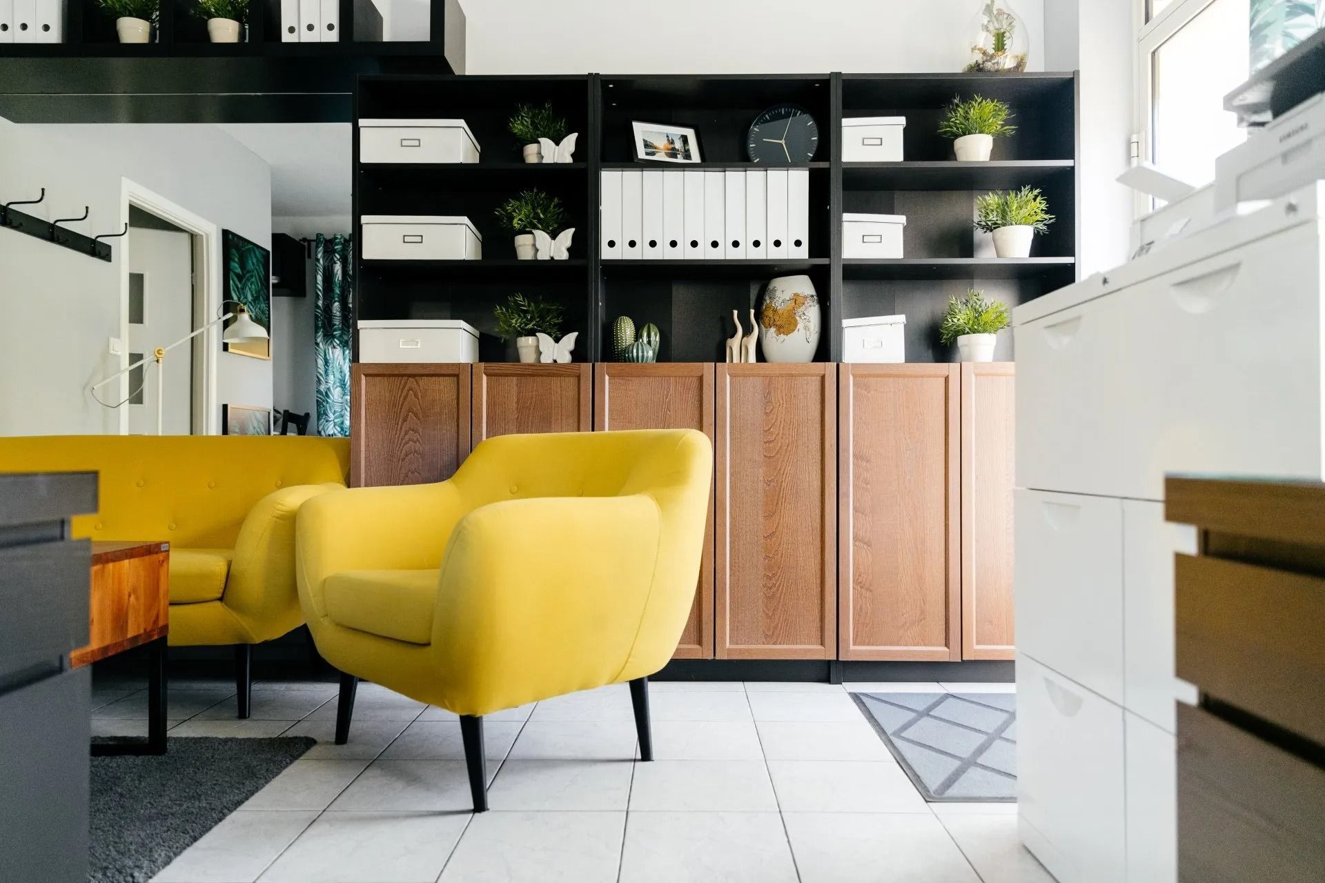 Modern living room with a mustard yellow sofa, wooden cabinets, and black shelving with plants and decor