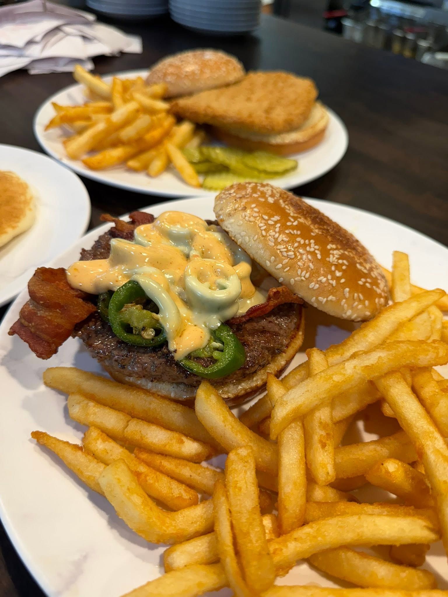Plates of burgers and French fries on a restaurant table, including a burger with melted cheese and jalapeños.
