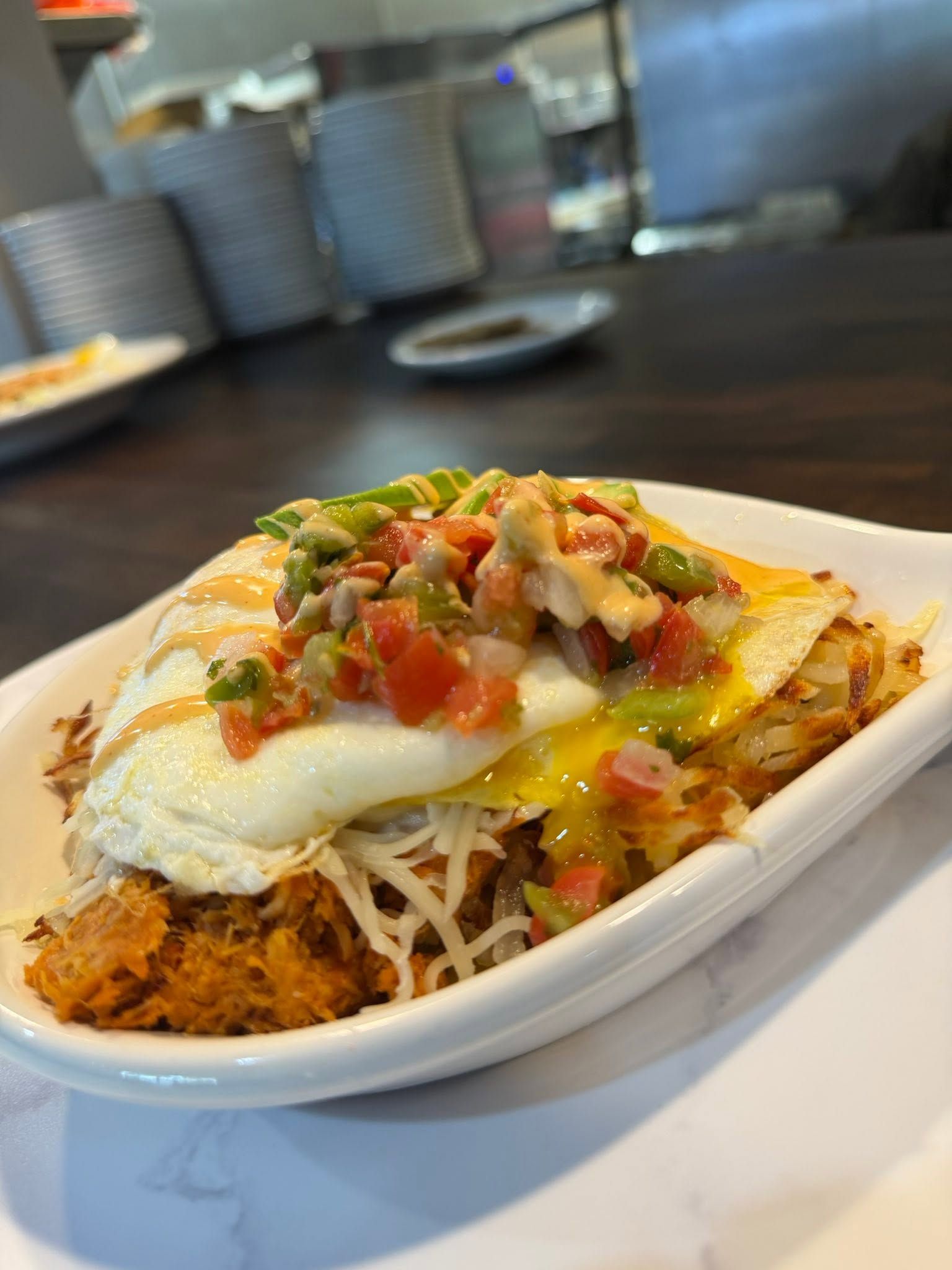 Loaded chilaquiles with green salsa, cheese, and eggs on a white dish at a restaurant counter