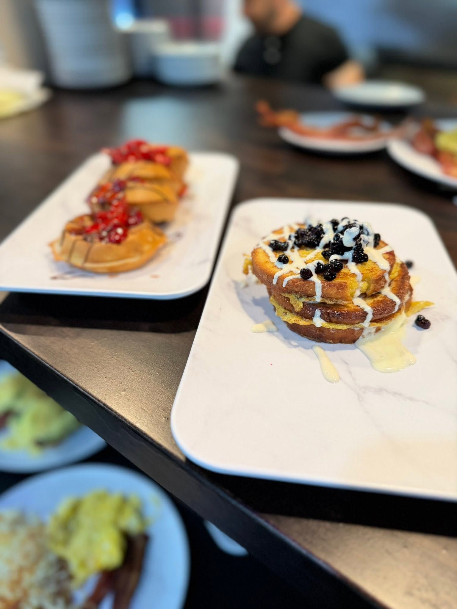 Two plated pastries topped with fruit, chocolate, and cream on a restaurant table
