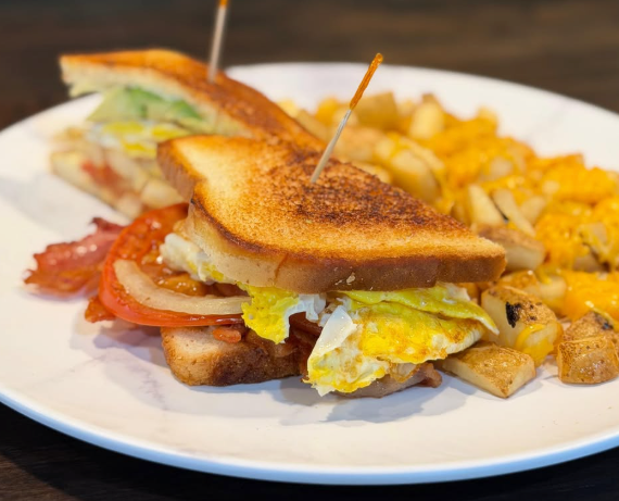 Grilled sandwich with tomato and lettuce on a white plate, served with potato cubes and chips