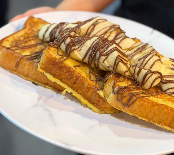 Two stuffed French toast slices topped with banana, chocolate drizzle, and syrup on a white plate