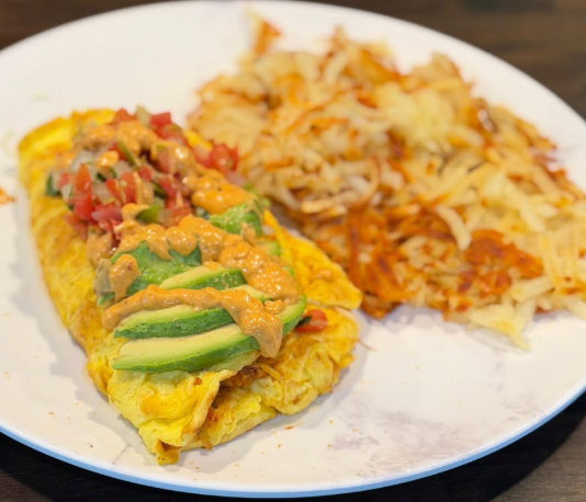 Omelette topped with avocado and salsa, served with hash browns on a white plate.