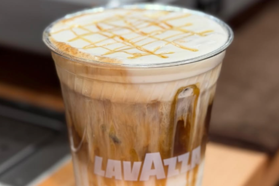 Iced caramel latte in a clear plastic cup with foam and caramel drizzle, Lavazza logo visible