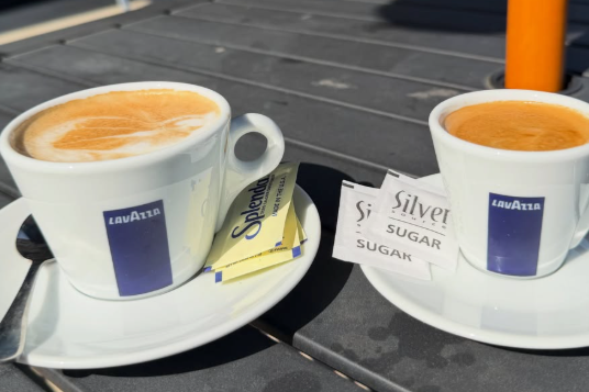 Two cups of coffee with sugar packets on saucers on a dark table