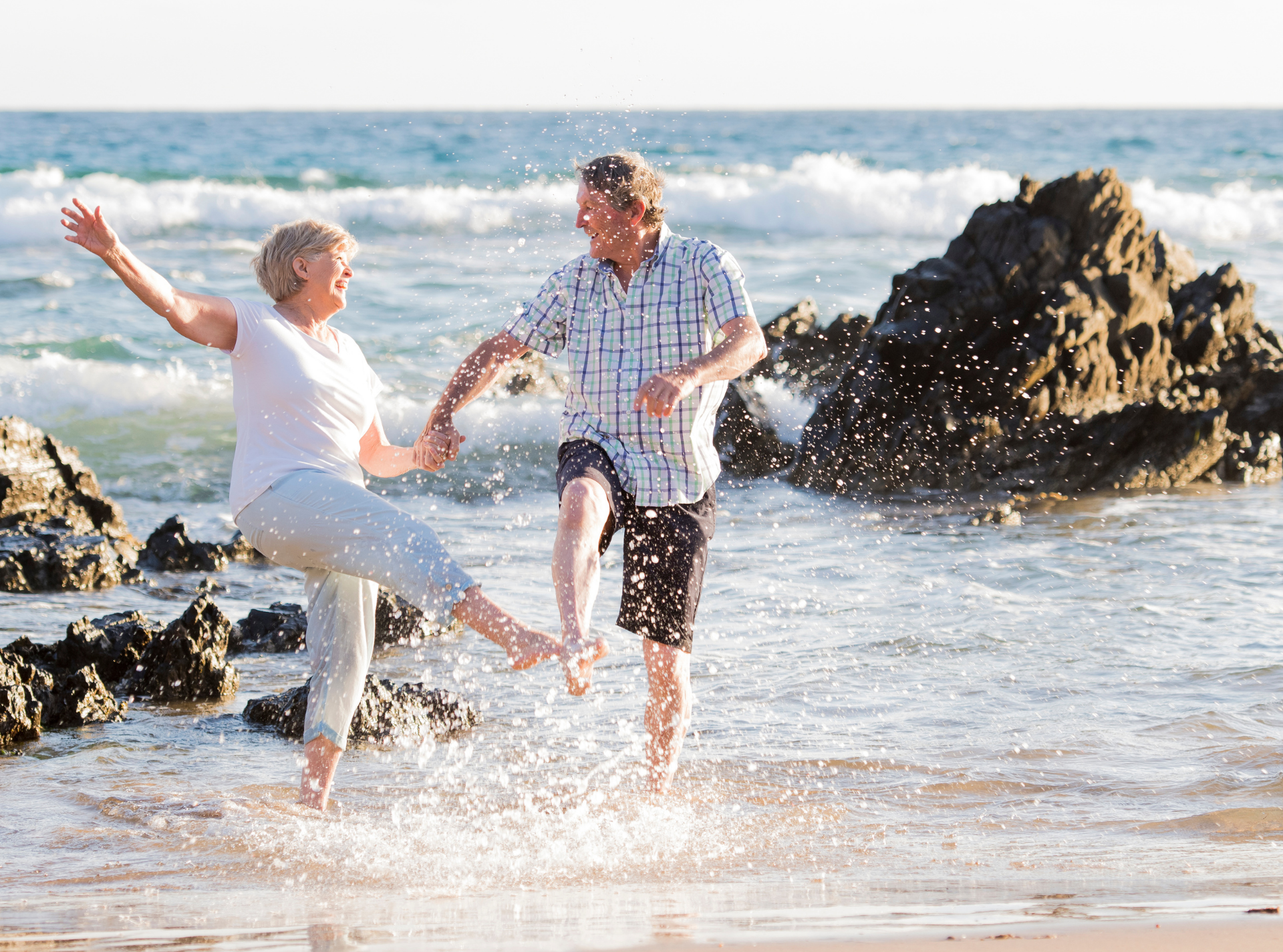 An elderly couple is playing in the water on the beach.