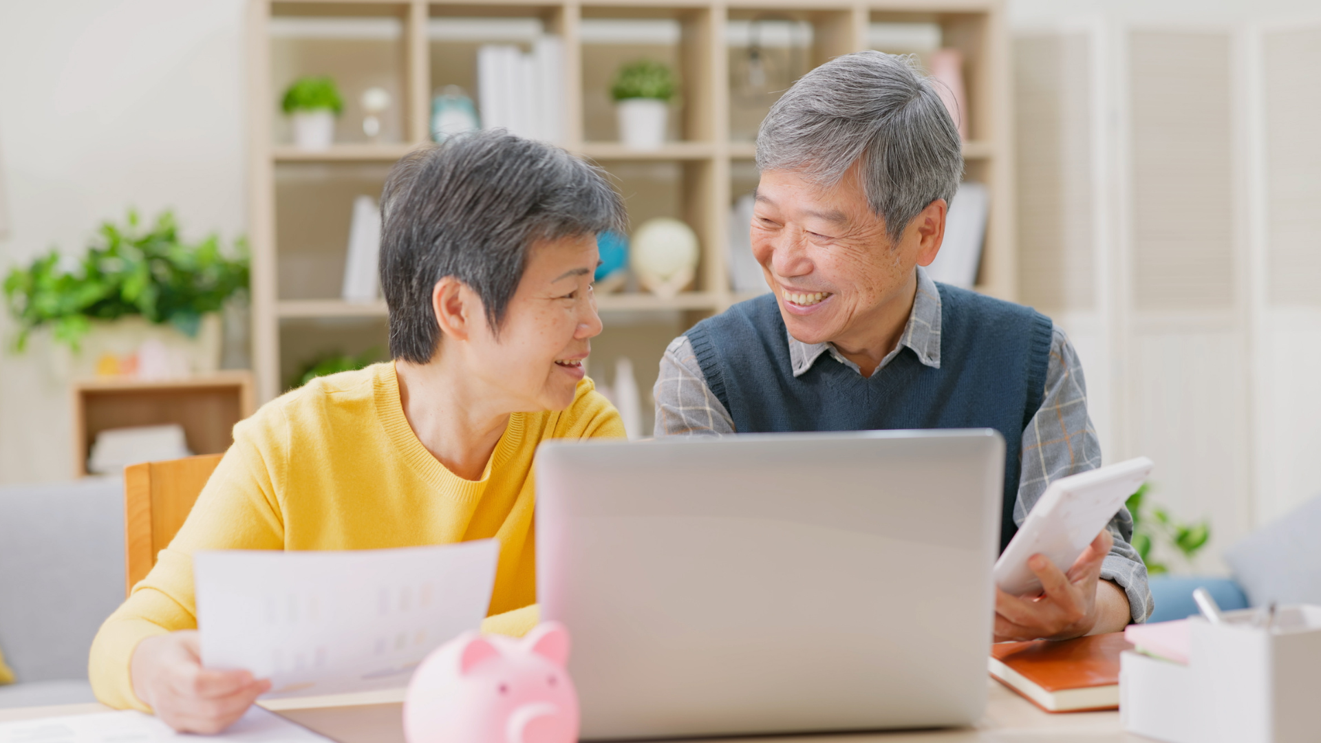 An elderly couple is sitting at a table looking at a laptop computer.