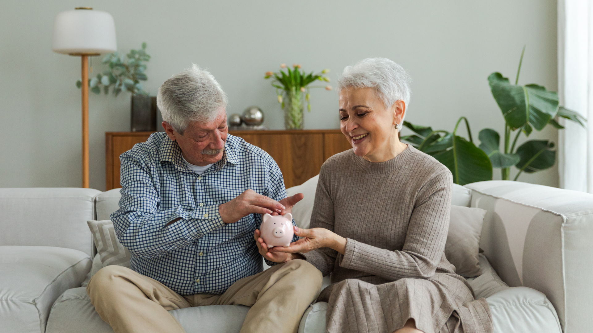 An elderly couple is sitting on a couch holding a piggy bank.