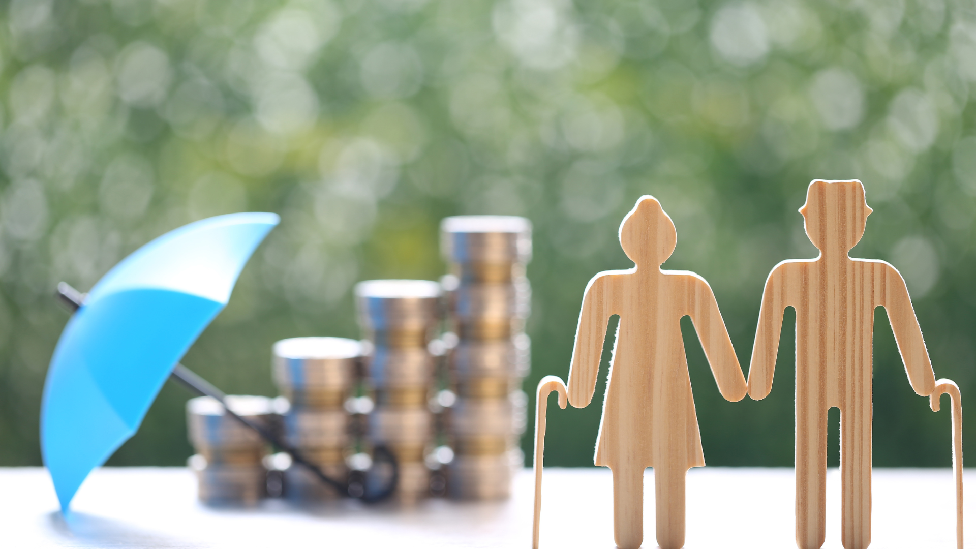 A wooden figure of an elderly couple holding hands next to a stack of coins and an umbrella.
