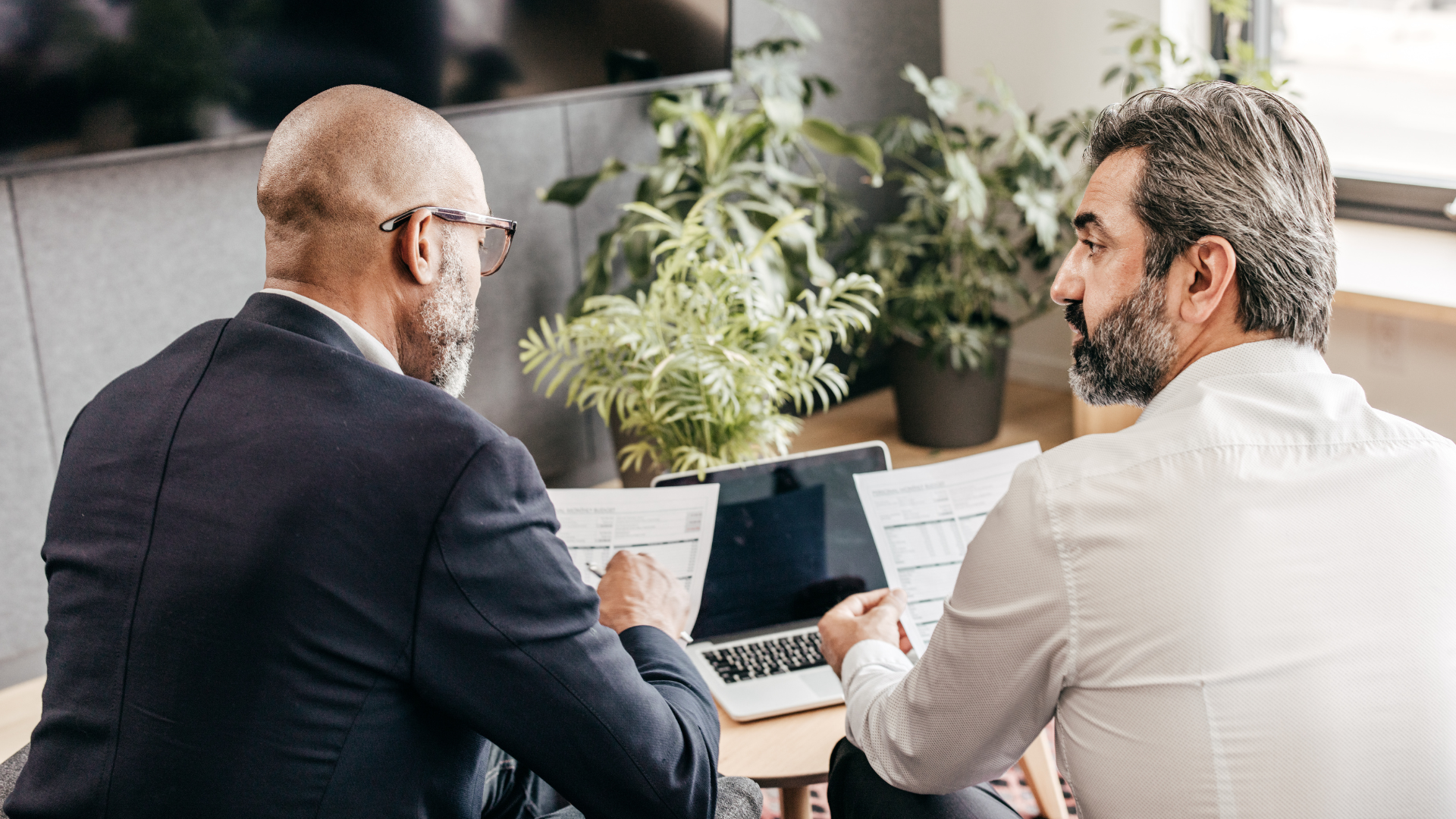 Two men are sitting at a table looking at a laptop.