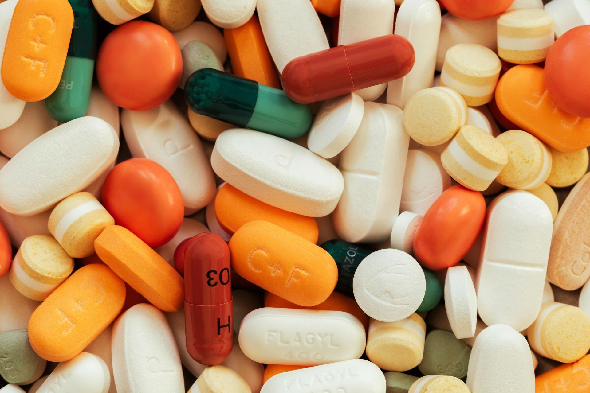 A close-up, top-down view of a scattered collection of various prescription pills and capsules of different colors and shapes.