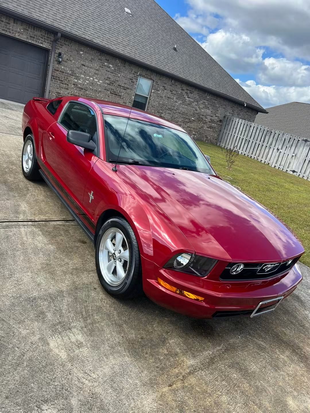 Red Ford Mustang parked on a driveway beside a brick house on a cloudy day