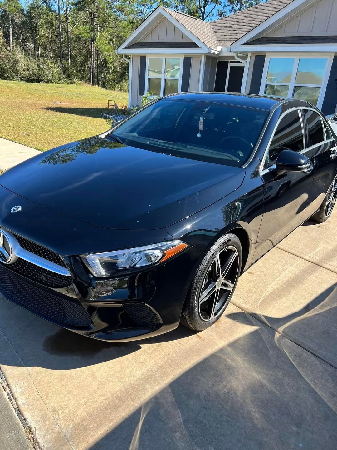 Black sedan parked in a driveway in front of a house on a sunny day