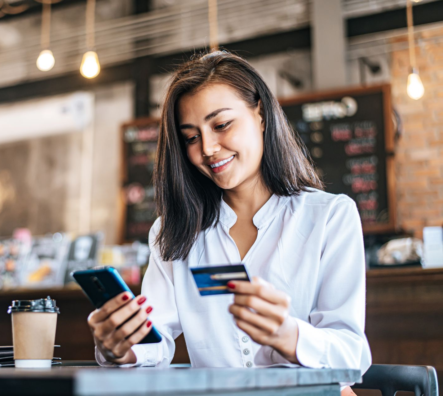 Woman holding a gold credit card, smiling, using a laptop, sitting on a couch.