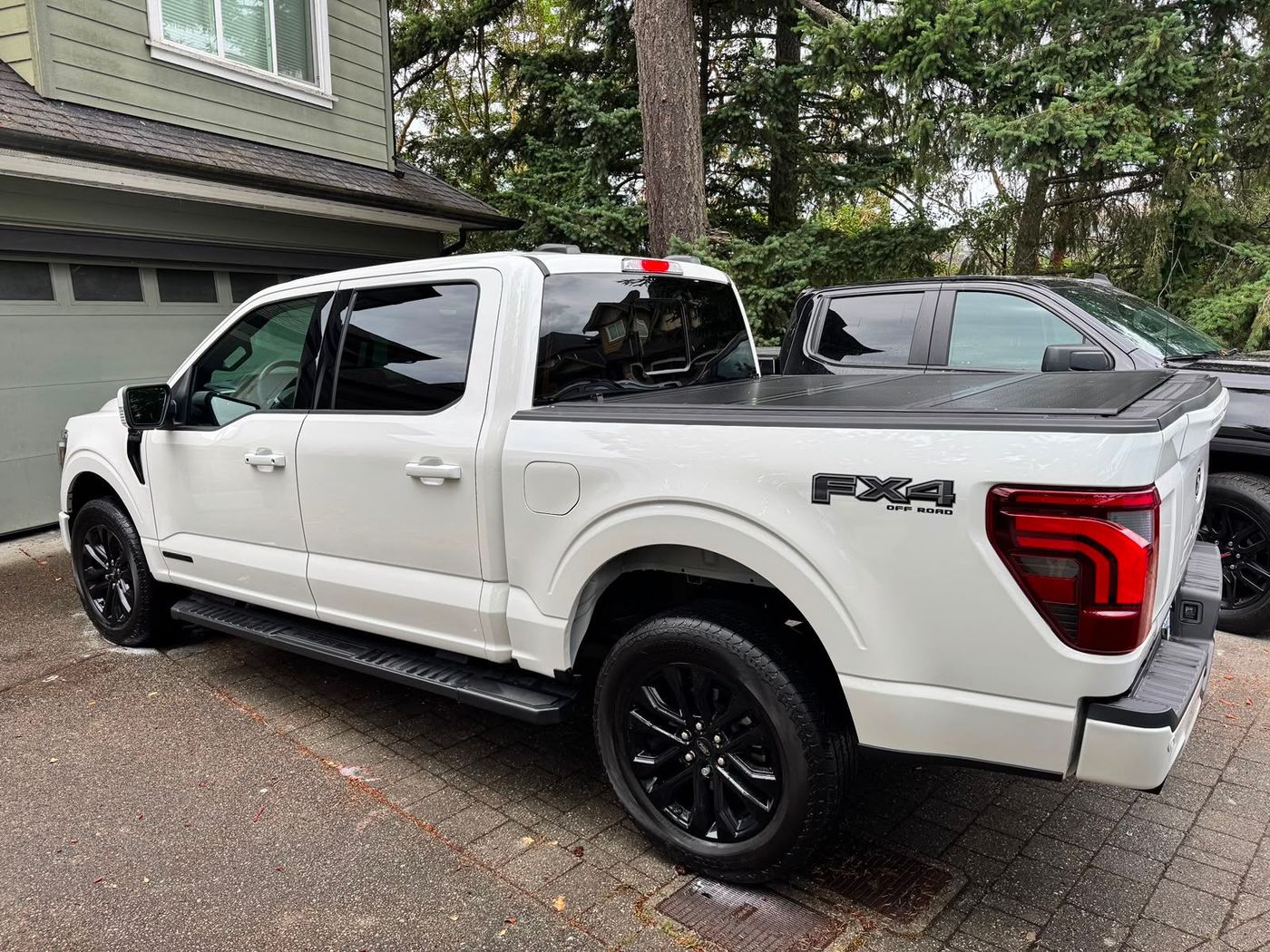 White Ford F-150 pickup truck parked in a driveway beside a house, rear three-quarter view