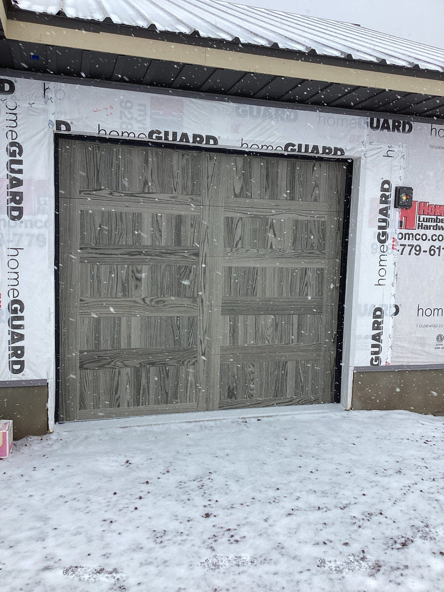 A garage door is sitting in the snow next to a house.