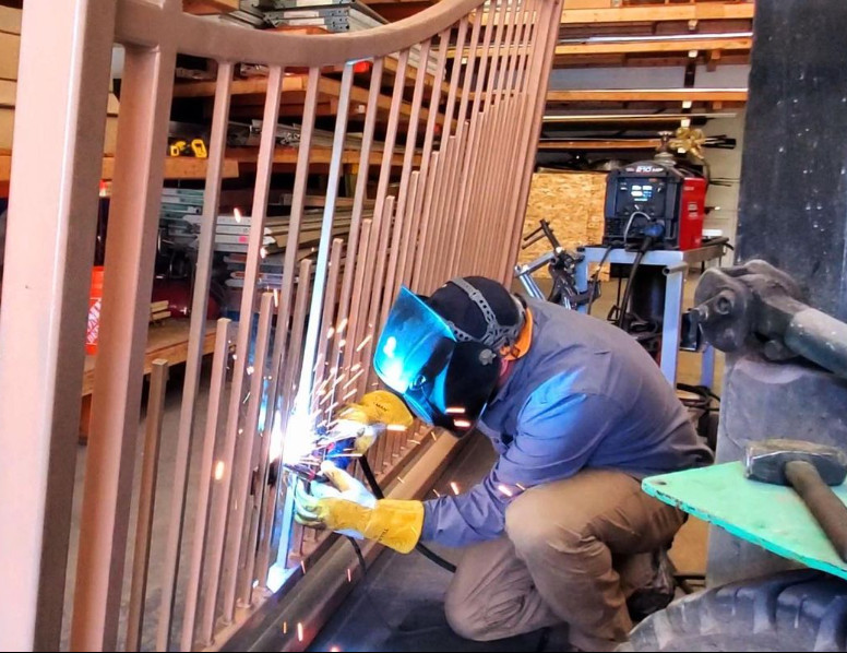 A man wearing a welding mask is welding a railing