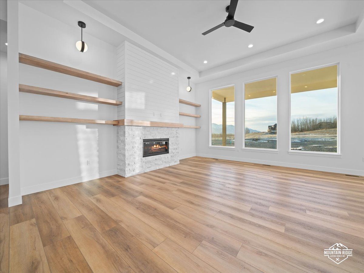 Bright empty living room with hardwood floors, white walls, built-in shelves, fireplace, and large windows.