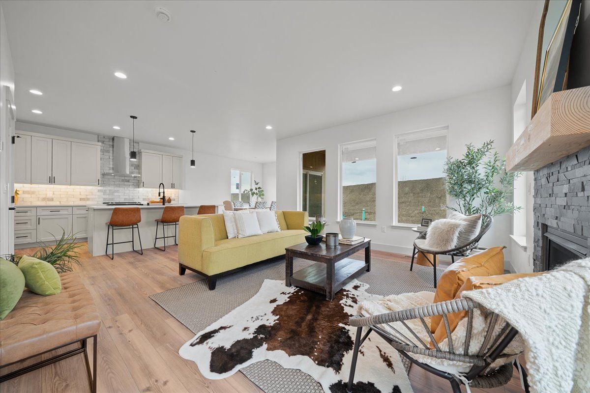 Bright modern living room with yellow sofa, fireplace, open kitchen, and large windows.