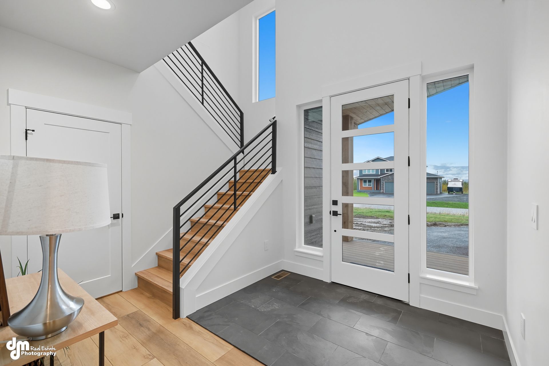 Bright entryway with staircase, white double doors, gray tile floor, and a lamp on a wood table